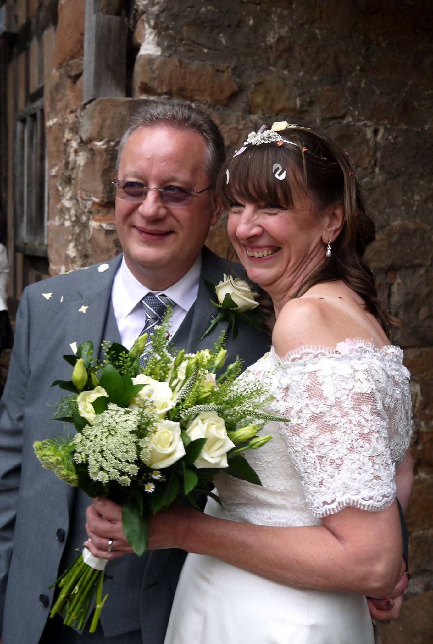 A middle aged couple on their wedding day, smiling as confetti is being thrown over them. 