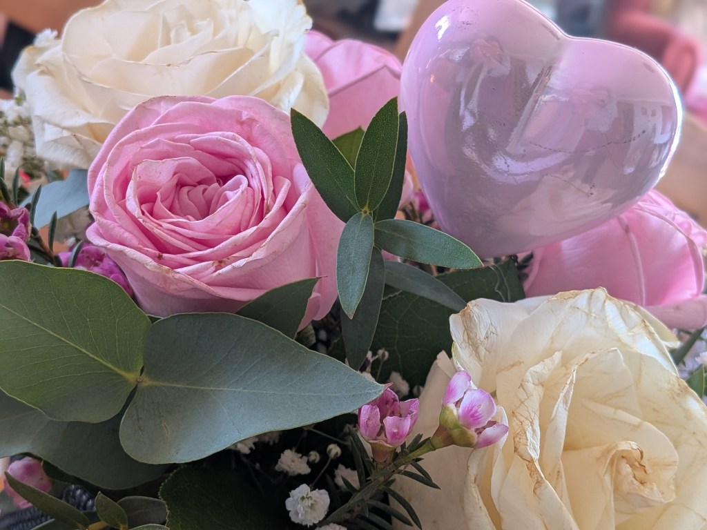 A bouquet of pink and cream flowers with a pink plastic heart. 